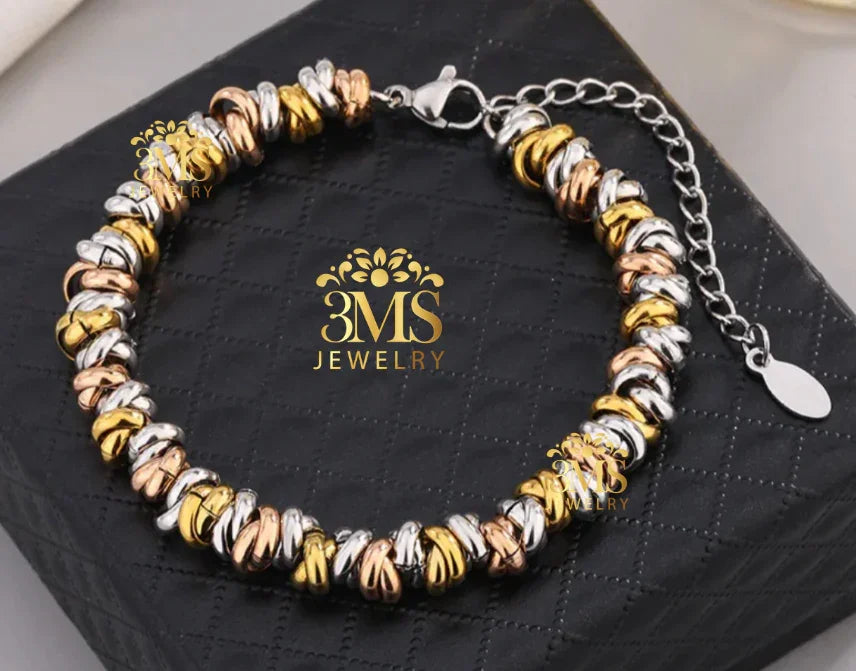 Tri-color twisted metal bracelet with adjustable chain on black textured jewelry box