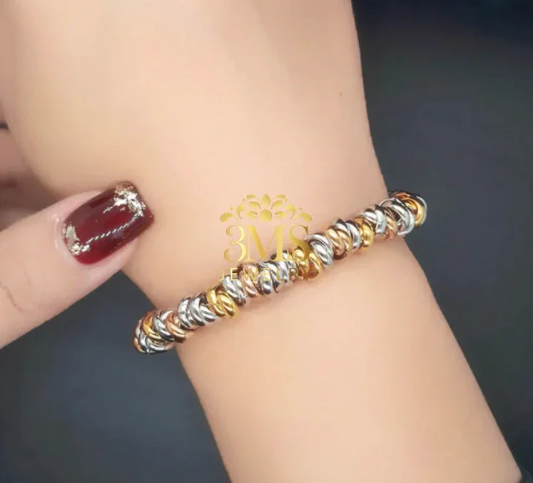 Close-up of wrist wearing a gold and silver twisted link bracelet with a dark background
