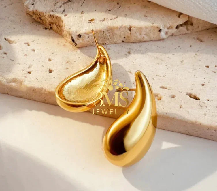 Elegant gold droplet-shaped earrings on textured beige stone surface