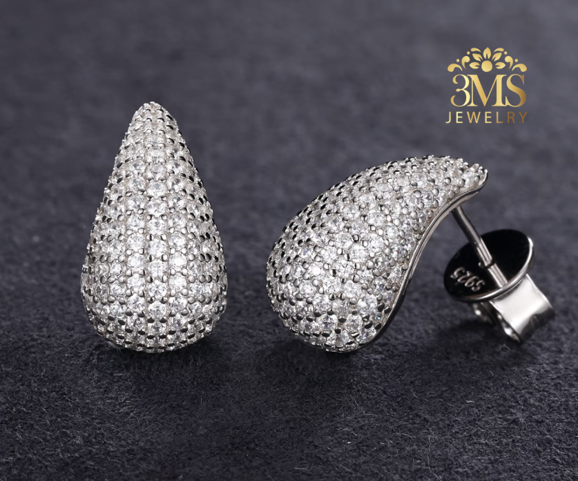 Teardrop-shaped silver earrings with clear stones on a dark background, featuring the 3MS Jewelry logo.