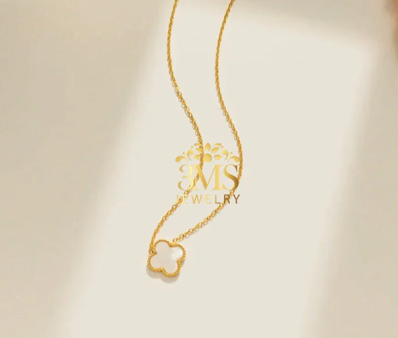 Elegant gold necklace with a clover-shaped pendant on a light beige background