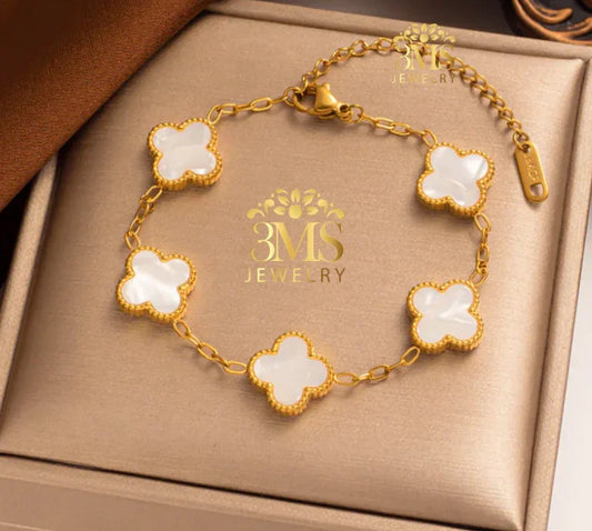 Gold chain bracelet with five white clover-shaped charms on a beige jewelry box