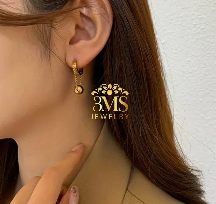 Close-up of a woman wearing a gold hoop earring with a hanging gold bead pendant