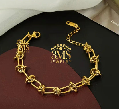 Gold chain link bracelet with decorative knots, adjustable clasp on black and brown background