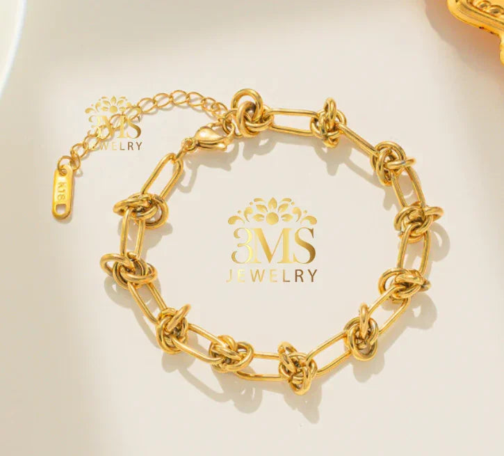 Gold chain link bracelet with intricate knot details on a cream background