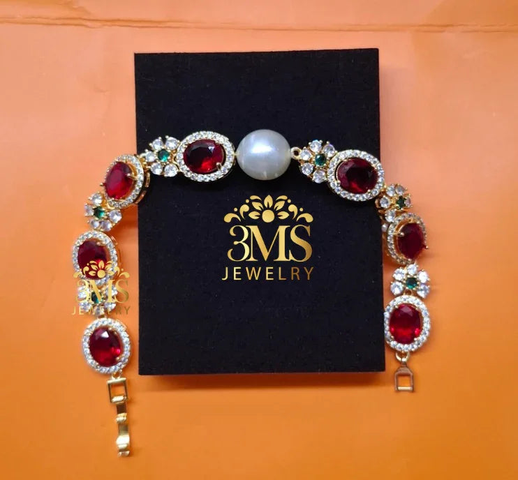 Elegant gold bracelet with oval red rubies, green and white gemstones, and a central pearl on black 3MS Jewelry box