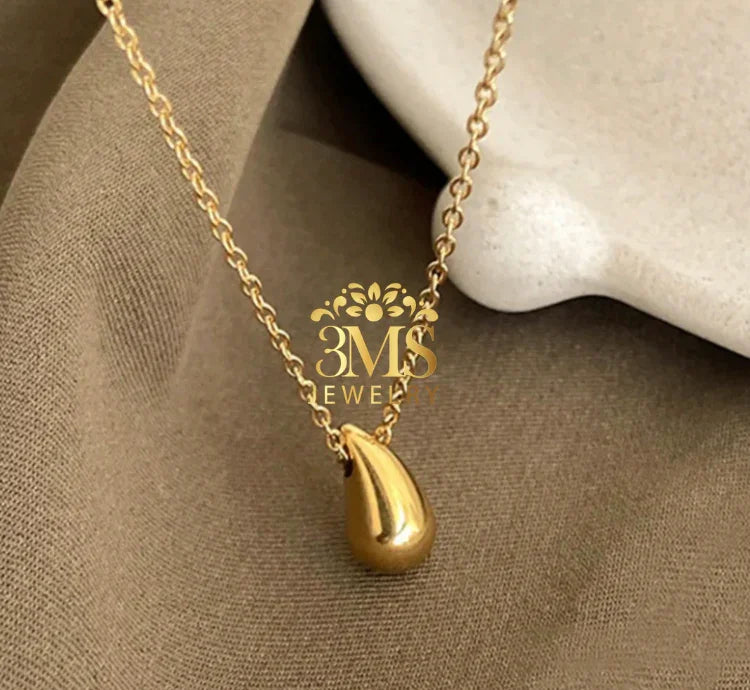 Gold teardrop pendant necklace on beige fabric background with 3MS Jewelry logo
