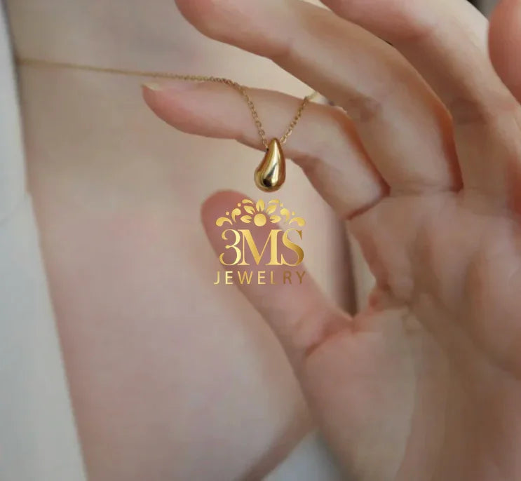 Close-up of hand holding gold teardrop pendant necklace from 3MS Jewelry