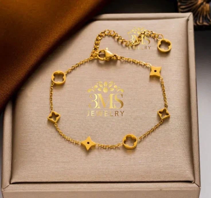 Delicate gold bracelet with flower and star-shaped charms on beige jewelry box
