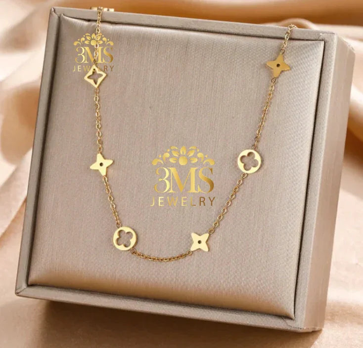 Elegant gold chain necklace with flower-shaped and quatrefoil charms in a beige jewelry box