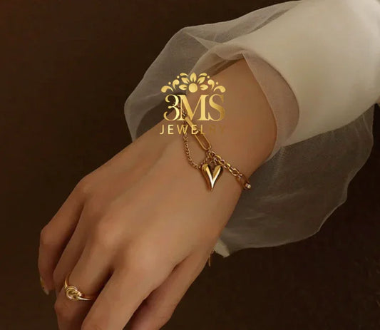 Gold sweetheart charm bracelet on wrist with sheer white sleeve, elegant jewelry accessory