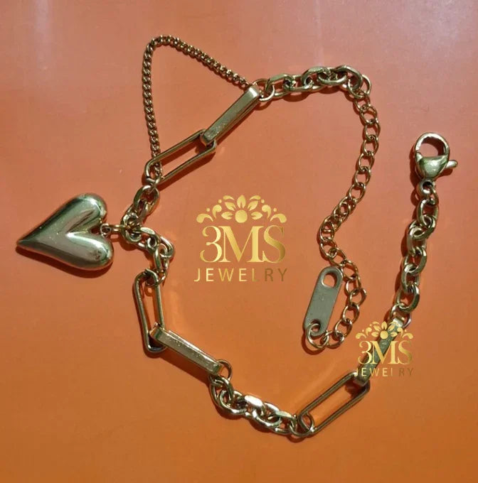 gold-tone bracelet with heart charm and mixed chain links laid on orange background