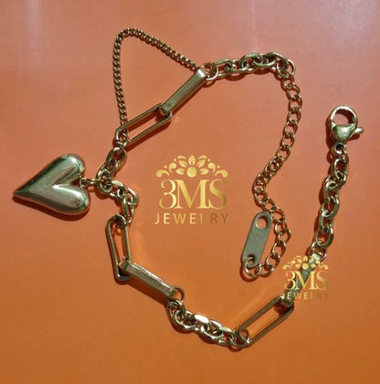 gold-tone bracelet with heart charm and mixed chain links laid on orange background