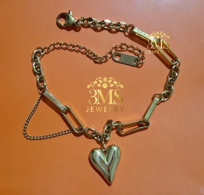 Gold bracelet with chunky chain and heart-shaped charm on orange background