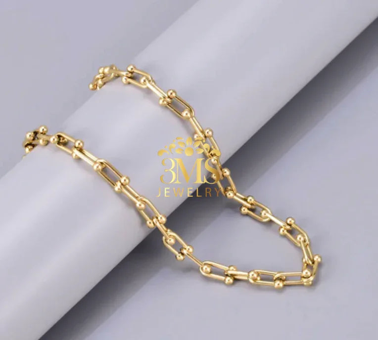 Gold chain necklace with bead details displayed on a white cylindrical prop, gray background