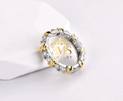 Elegant silver eternity ring with gold prongs and clear gemstones on white surface