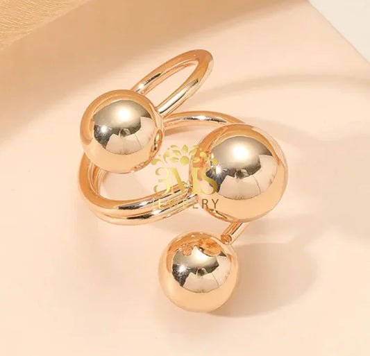 Modern gold ring with three polished spherical beads on a beige surface